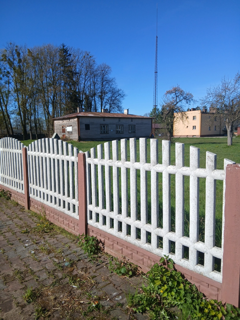 Mycie ogrodzeń – białe betonowe ogrodzenie z różowymi słupkami przy chodniku i zielonym trawniku