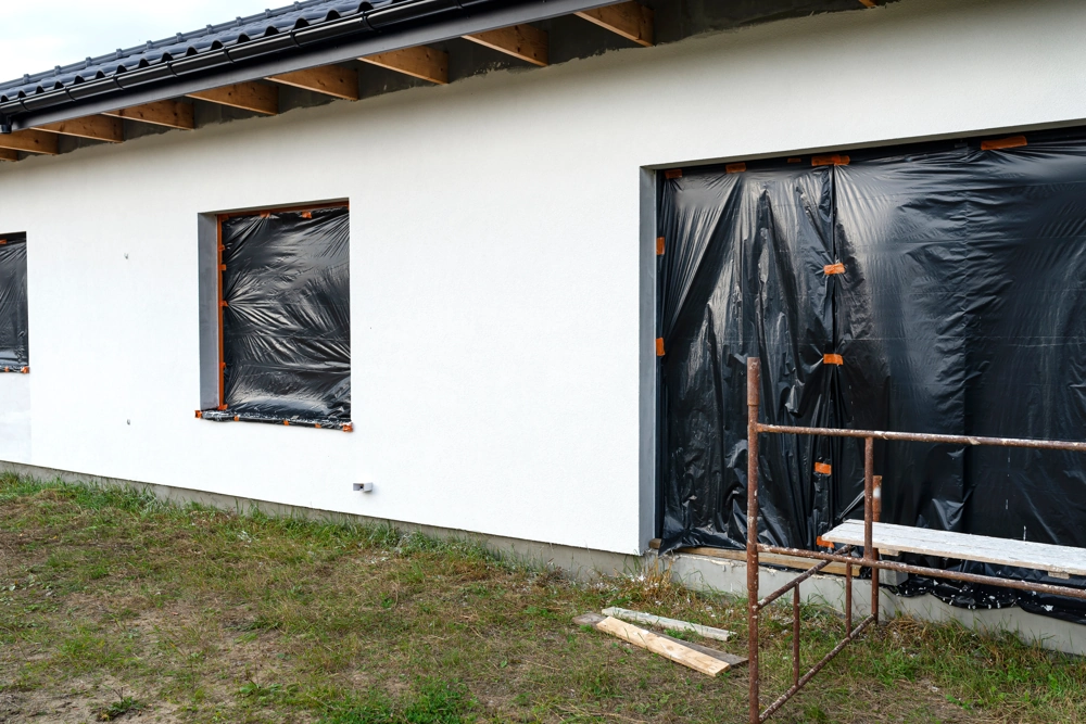 Impregnacja elewacji – biała ściana budynku z oknami osłoniętymi folią i rusztowaniem